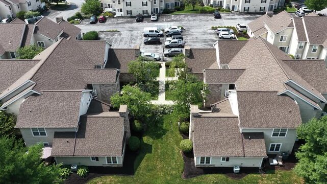 Mirrored townhouse rooftops frame landscaped courtyard path in Elizabethtown, Pennsylvania, parked cars fill lot as green lawns separate symmetrical housing units. Aerial drone top down shot