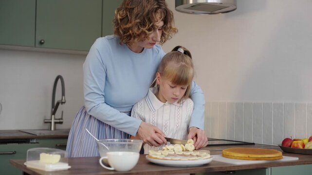 Mother and daughter bake layered cake together in cozy sunlit kitchen, 25 fps