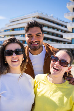 Vertical. Small group portrait of friends smiling in a bright residential district with palm trees and modern architecture, capturing a friendly social lifestyle scene.