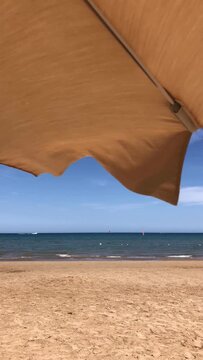 Beige beach umbrella waving in the wind on a sunny day with blue sea and sand beach background