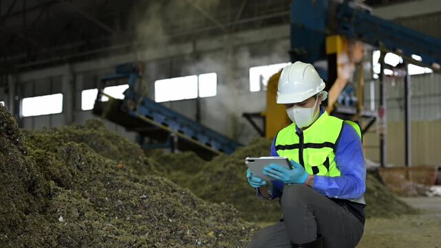 Engineer in safety gear using a digital tablet to supervise industrial waste sorting and plastic recycling