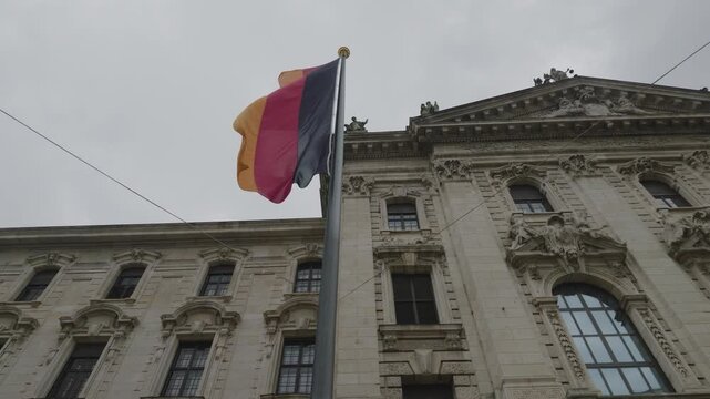German national flag waves in front of ornate historic building  in Munich 