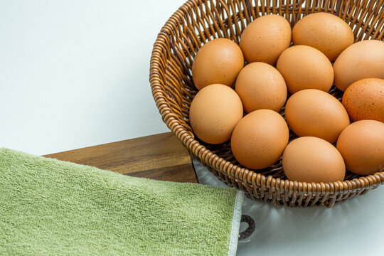 Wicker basket full of brown eggs next to folded kitchen towel isolated on white