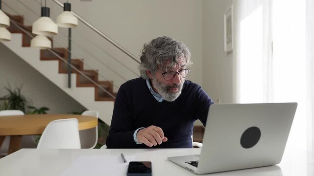 Excited mature businessman celebrating success with laptop at home