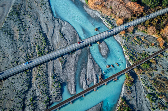 New Zealand - 09 July 2021: View of a turquoise river flowing under a road bridge and a railway bridge, surrounded by gravel riverbeds and sparse vegetation.