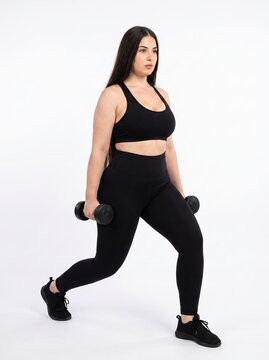 Confident woman doing dumbbell workout in athletic outfit against neutral background