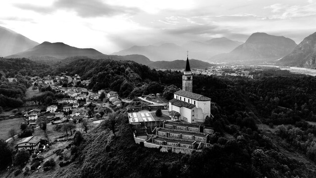 Aerial view of an ancient stone parish church with a bell tower on a misty hilltop at sunset, Cesclans, Carnia, Friuli-Venezia Giulia, Italy