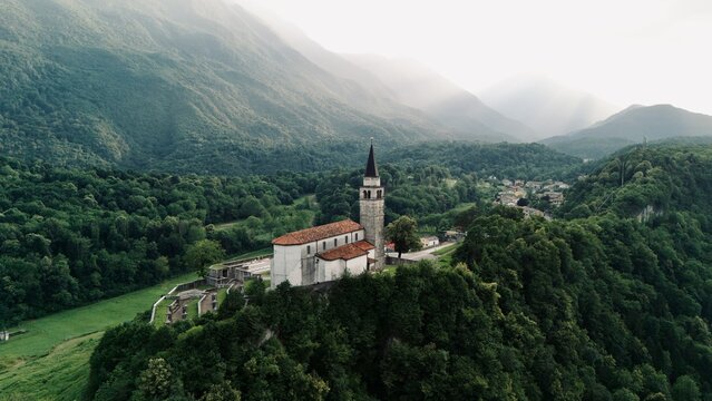 Aerial view of an ancient stone parish church on a rocky hill above a village at sunset, Cesclans, Carnia, Friuli-Venezia Giulia, Italy