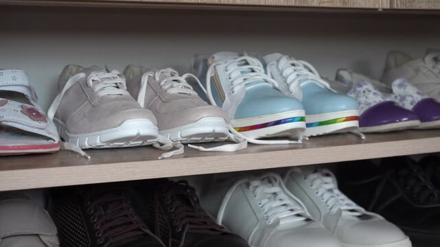 Various shoes and sneakers on wooden shelves in wardrobe close up, Home shelf with casual shoes close-up.