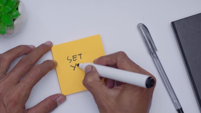 A man writing SET YOUR PLAN on orange sticky note