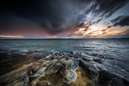 New Zealand - 26 April 2021: View of a rocky shoreline under a dramatic stormy sky at sunset with dark clouds and fading light over the water.