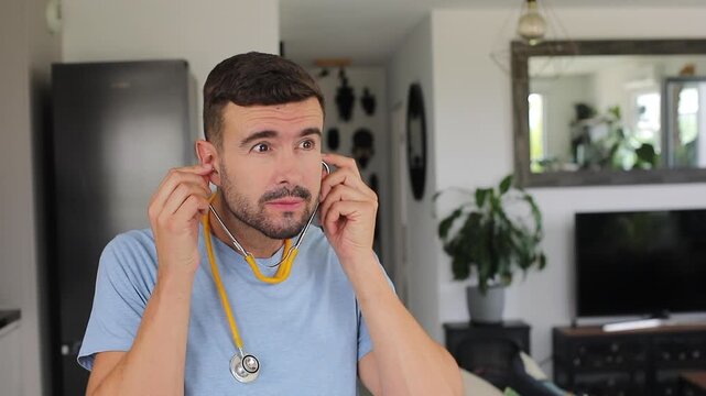 Man putting on a stethoscope at home to listen to his own heart with an anxious expression.