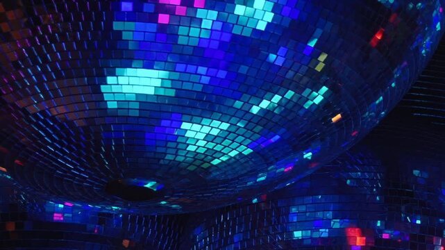 Multiple mirrored disco balls shimmer with brilliant red, blue, and green light in a dark club setting. The rotating reflections create a dynamic, electrifying party ambiance.