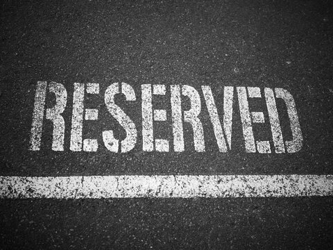 White stencilled RESERVED marking on dark asphalt with painted line, black and white