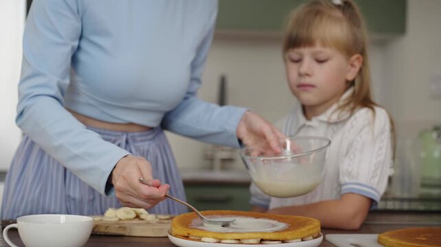 Mother and daughter bake layered cake together in cozy sunlit kitchen, 25 fps