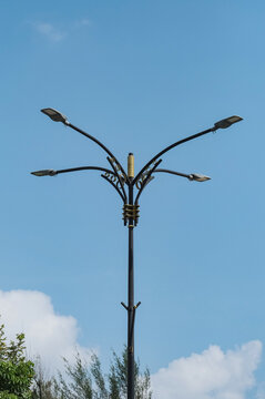 Ornamental four-arm LED street lamppost featuring decorative golden accents against a blue sky background.  Modern urban infrastructure and outdoor energy-efficient lighting concept