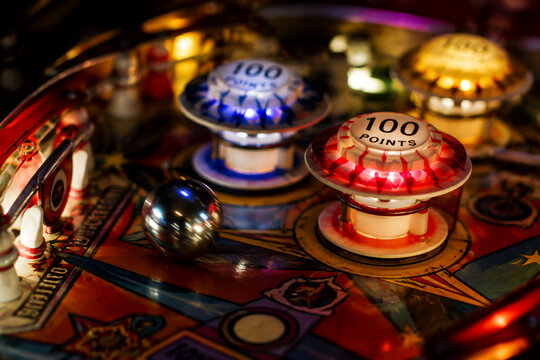 Close-up inside a vintage pinball machine, a silver ball near colorful bumpers.