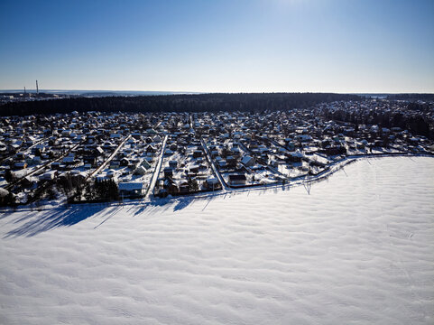 Aerial drone view of a snowy suburban community featuring cozy residential dachas and small private houses nestled in a tranquil winter landscape under a clear blue sky