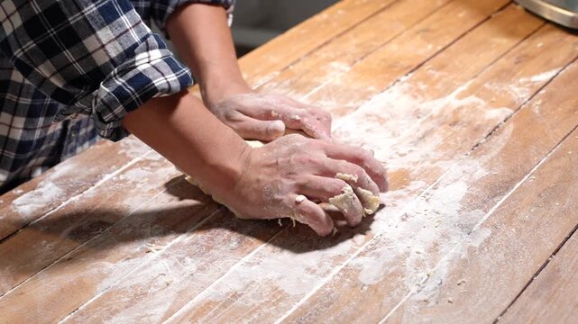 Close up of hands kneading dough on a floured wooden table in a home kitchen, showing fresh baking, cooking skills, and handmade food preparation.