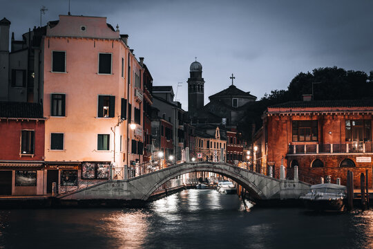 Venice, Italy - 05 October 2022: View of a stone bridge over a canal in Venice at dusk, with historic buildings and reflections on the water.