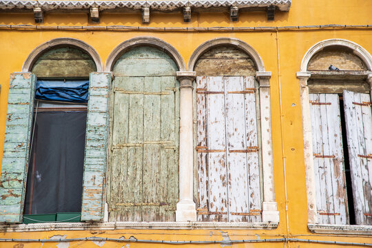 04 October 2022: View of weathered wooden shutters on arched windows of a yellow building.