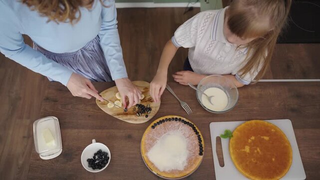 Mother and daughter bake layered cake together in cozy sunlit kitchen, 25 fps