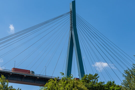 Cable stayed bridge pylon and steel cables against blue sky with container truck driving on road, infrastructure and logistics concept