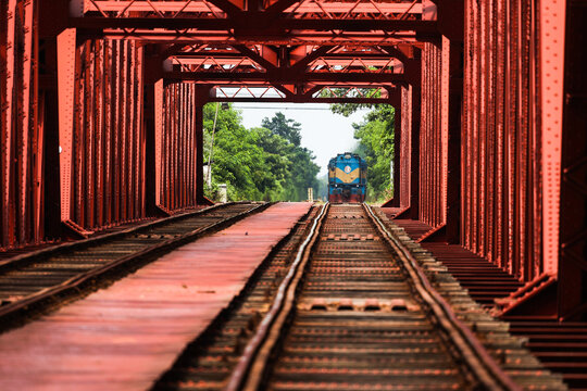 Pabna, Bangladesh - 17 August 2025: View of the iconic red steel truss of the Hardinge Bridge with a train approaching in the distance.