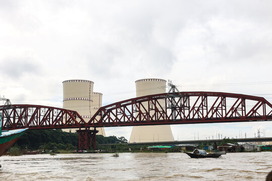 Pabna, Rajshahi Division, Bangladesh - 17 August 2025: View of the red steel truss bridge over the river with cooling towers of the Rooppur Nuclear Power Plant in the background.