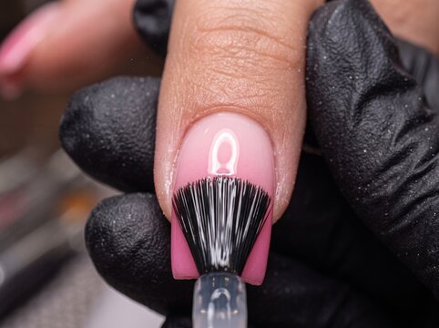 Applying glossy top coat on pink gradient acrylic nail with professional brush