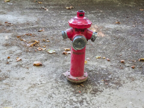 Bright red fire hydrant standing firmly on a dusty gravel ground surface captured in natural daylight showing detailed metallic construction and industrial safety equipment design