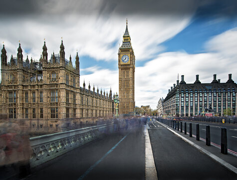 United Kingdom - 26 April 2023: View of the Elizabeth Tower, commonly known as Big Ben, and the Palace of Westminster under a dramatic cloudy sky with motion-blurred pedestrians on the bridge.
