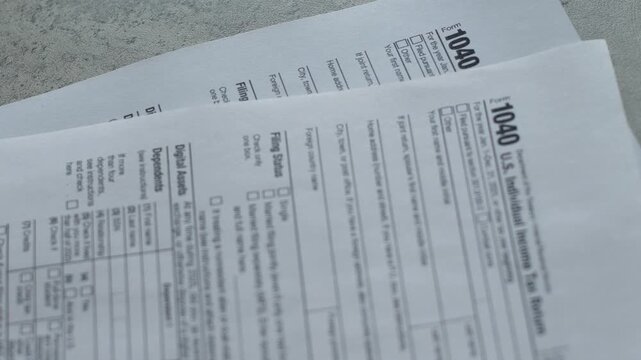 Close-up shot of official US Individual Income Tax Return Form 1040 blank documents for 2025. Stack of paper federal tax forms lying on a grey desk during tax season