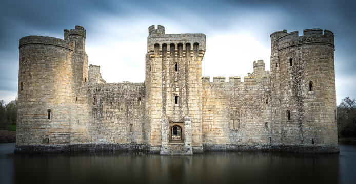 Bodiam, United Kingdom - 18 April 2023: View of Bodiam Castle, a 14th-century moated castle with stone walls and towers reflected in the surrounding water under a cloudy sky.