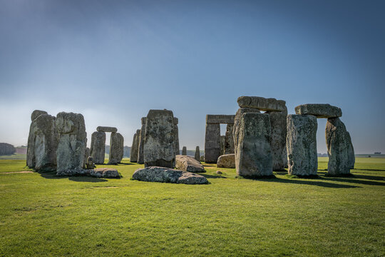 United Kingdom - 20 April 2023: View of the ancient stone circle of Stonehenge standing on a grassy plain under a clear blue sky.
