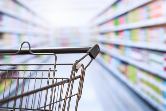 Shopping cart in a supermarket aisle with blurred shelves in the background, suggesting grocery shopping and retail buying