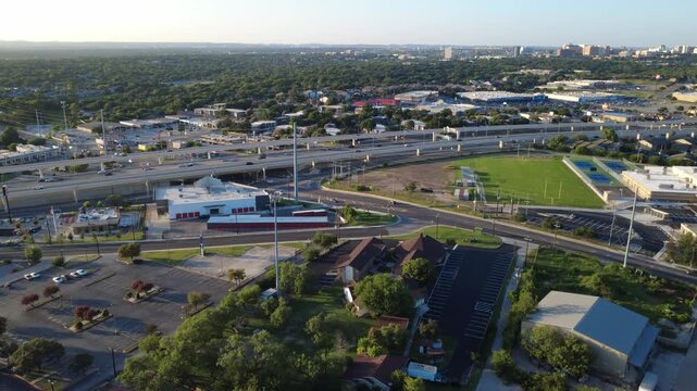Commercial parking tarmacs, campus athletics border Evers Road near Loop 410 across Bexar County region. Paved vehicle lots frame multi level highway viaducts across San Antonio, Texas