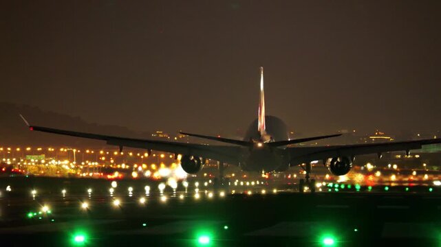 Dramatic back perspective of commercial passenger jet airliner touching down on airport runway at night. Airplane wheels emit distinct puff of friction smoke upon making contact with tarmac