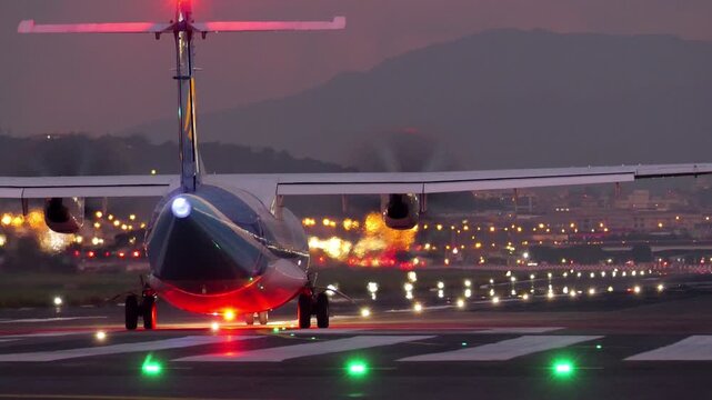 Tight telephoto rear view of twin-turboprop airliner at end of runway, preparing for departure at late evening. Spinning propellers and turbine exhaust create visible heat-haze distortion