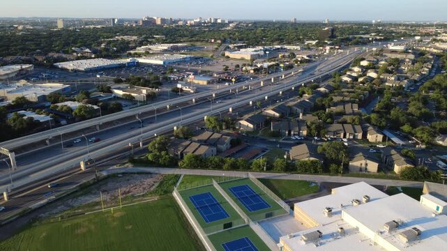 Hardcourt blue tennis courts, school football fields border Loop 410 near Neff Middle School in Bexar County. Campus recreation grounds frame elevated freeway ramps in San Antonio, Texas