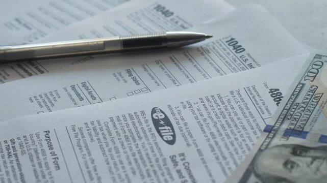 Close-up shot of US tax Form 1040 and Form 4868 with a metallic pen and a stack of hundred-dollar bills. Official IRS documents prepared for filing personal income tax returns 
