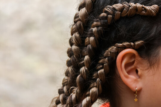 Braided hair close up showing dark textured hairstyle and ear with gold earring against soft outdoor background