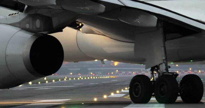 Tight telephoto view of commercial wide-body airliner turning on taxiway during evening twilight. Rear view highlights massive jet engine cowl, extended wing flaps, and heavy main landing gear wheels