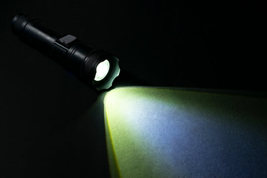 A black LED tactical flashlight with illuminated beam and multi-color flare effect on a textured dark background.