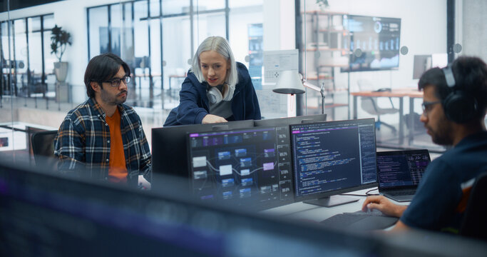 Caucasian Woman Developer With Platinum Hair and Headphones Explains Source Code to a Hispanic Male Engineer While Another Programmer Types on a Laptop, Building Software in a Diverse Office.