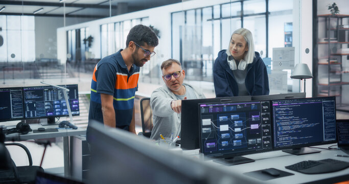Multiracial Software Engineers, Including an Indian Man, a Caucasian Man, and a Blonde Caucasian Woman With Headphones, Discuss Program Code and Data Flow Diagrams on Multiple Monitors in Tech Office