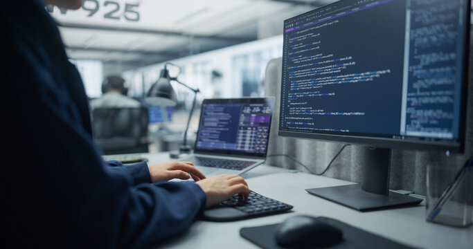 Over the Shoulder Shot of an Unrecognizable Software Engineer Writing Program Code and Sql Queries on a Desktop Computer and Laptop, Developing Backend Systems in an Office With Tech Specialists.
