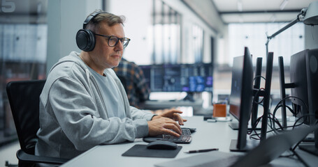 Fototapeta premium Portrait of a Concentrated Middle Aged Caucasian Male Software Developer in Glasses and Headphones Writing Program Code on a Desktop Computer, Building Applications With a Diverse Team in an Office.