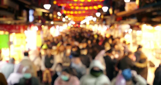 Rapid and chaotic rush of shoppers moves quickly past glowing market stalls and neon lights under rows of red lanterns on Dihua Street in Taipei. Intentional blurred view and fast-paced time lapse