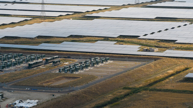 Aerial view of a large solar farm with rows of photovoltaic panels and battery storage containers in the countryside of Faversham, England, United Kingdom.
